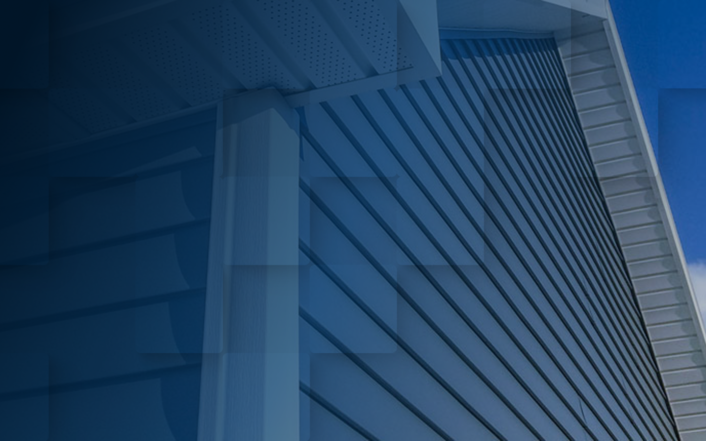 Close-up view of a house’s exterior corner with blue vinyl siding and a white roof soffit, photographed from a low angle against a partly cloudy Mississippi sky—an example of Hayman’s Roofing & Construction craftsmanship.